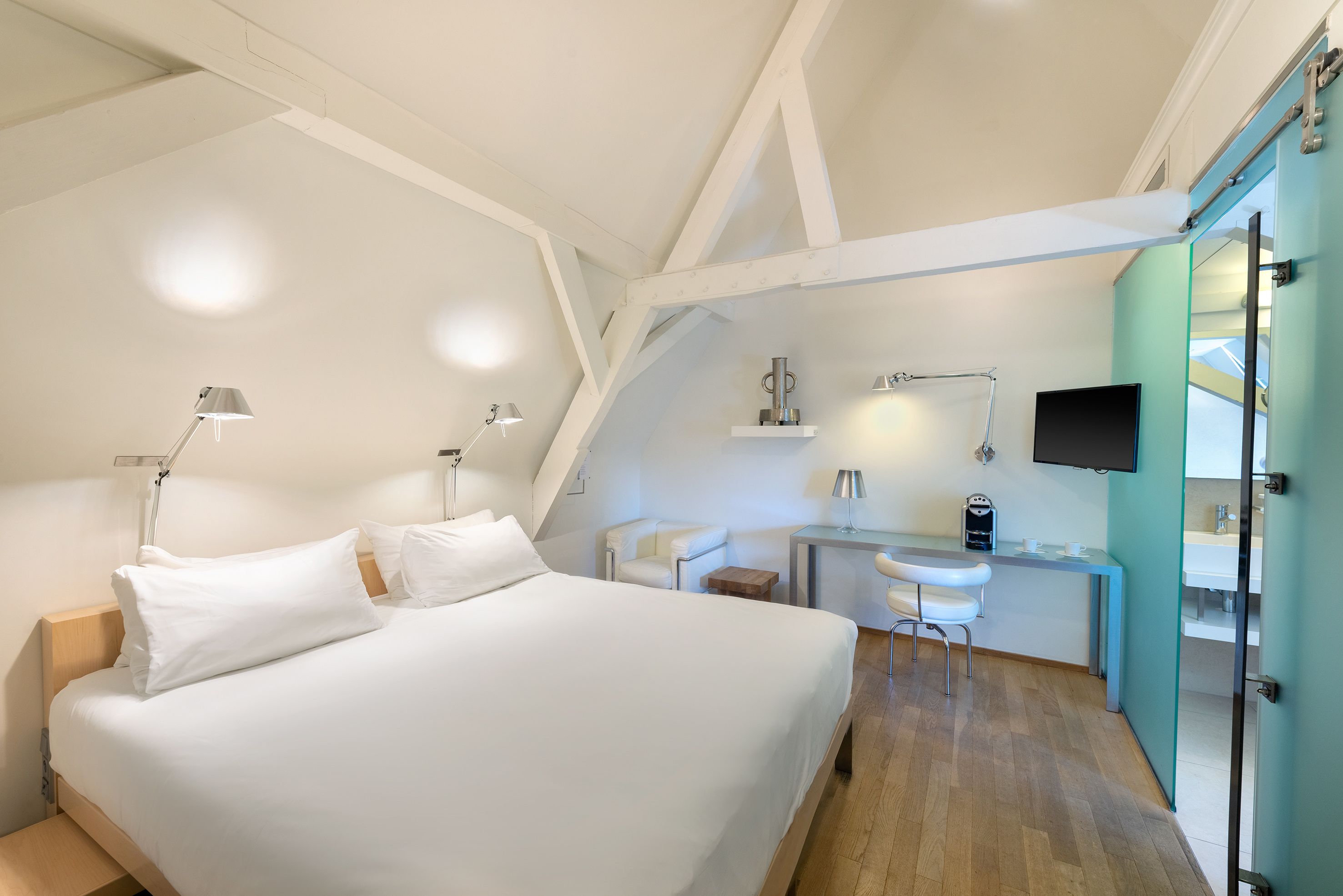 A modern hotel room with a large bed, a desk, and a TV.