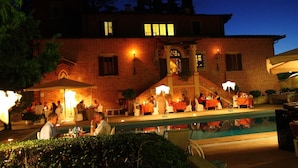 Un'area pranzo all'aperto con tavoli e sedie, una piscina e un edificio in mattoni sullo sfondo.