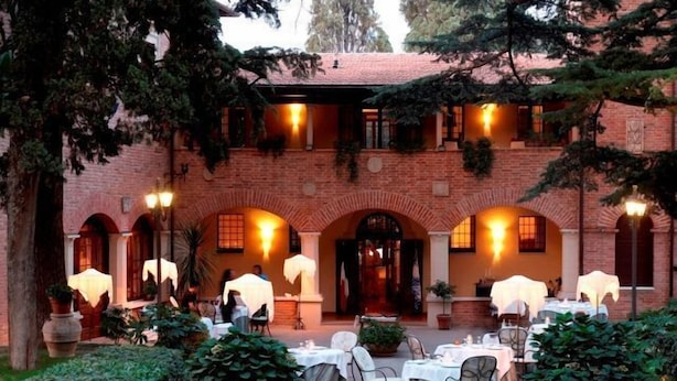 Un cortile con tavoli e sedie, circondato da muri in mattoni e portali ad arco.