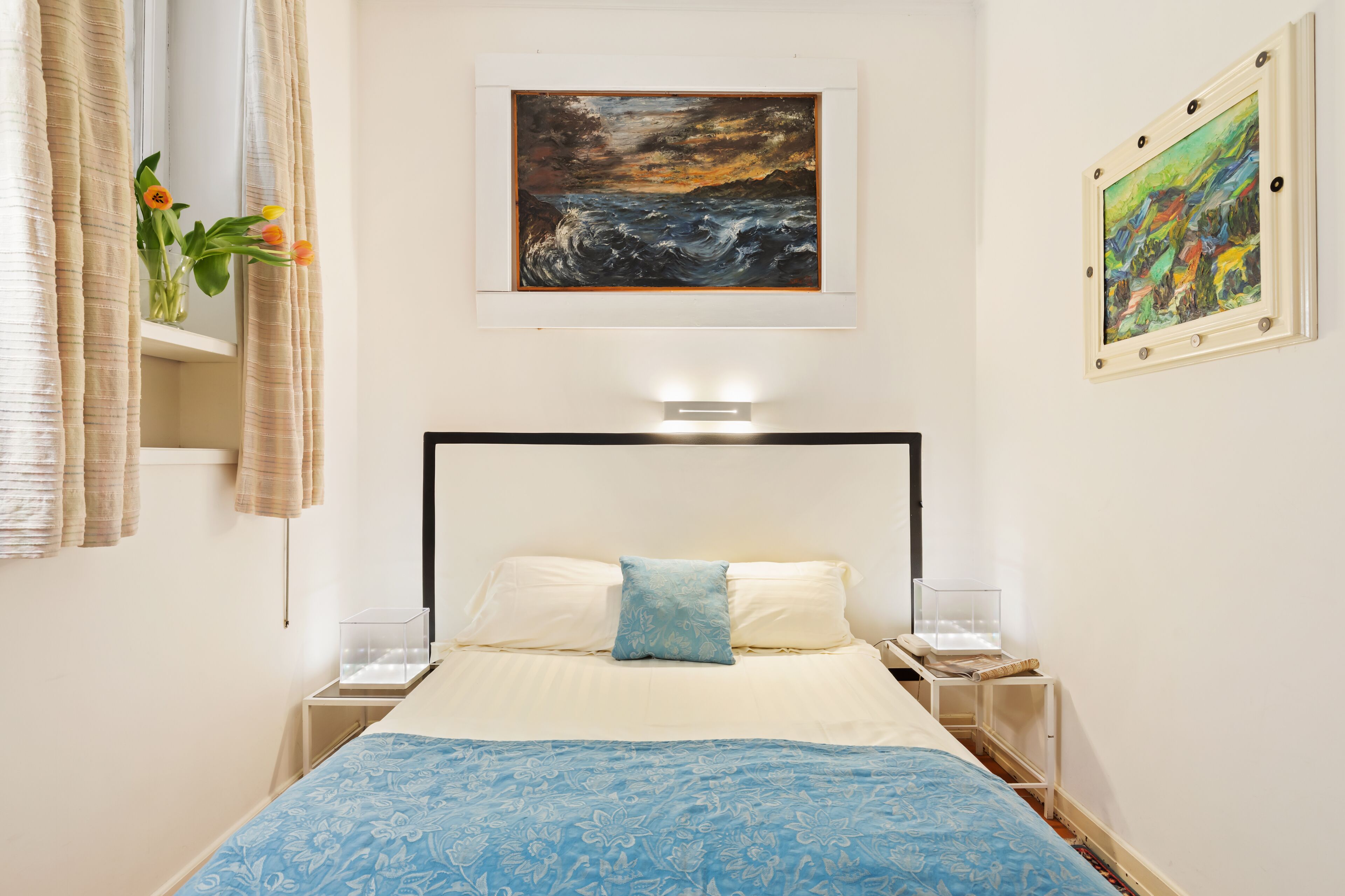 Una camera da letto con un letto, un comodino, una lampada e due quadri alle pareti.
