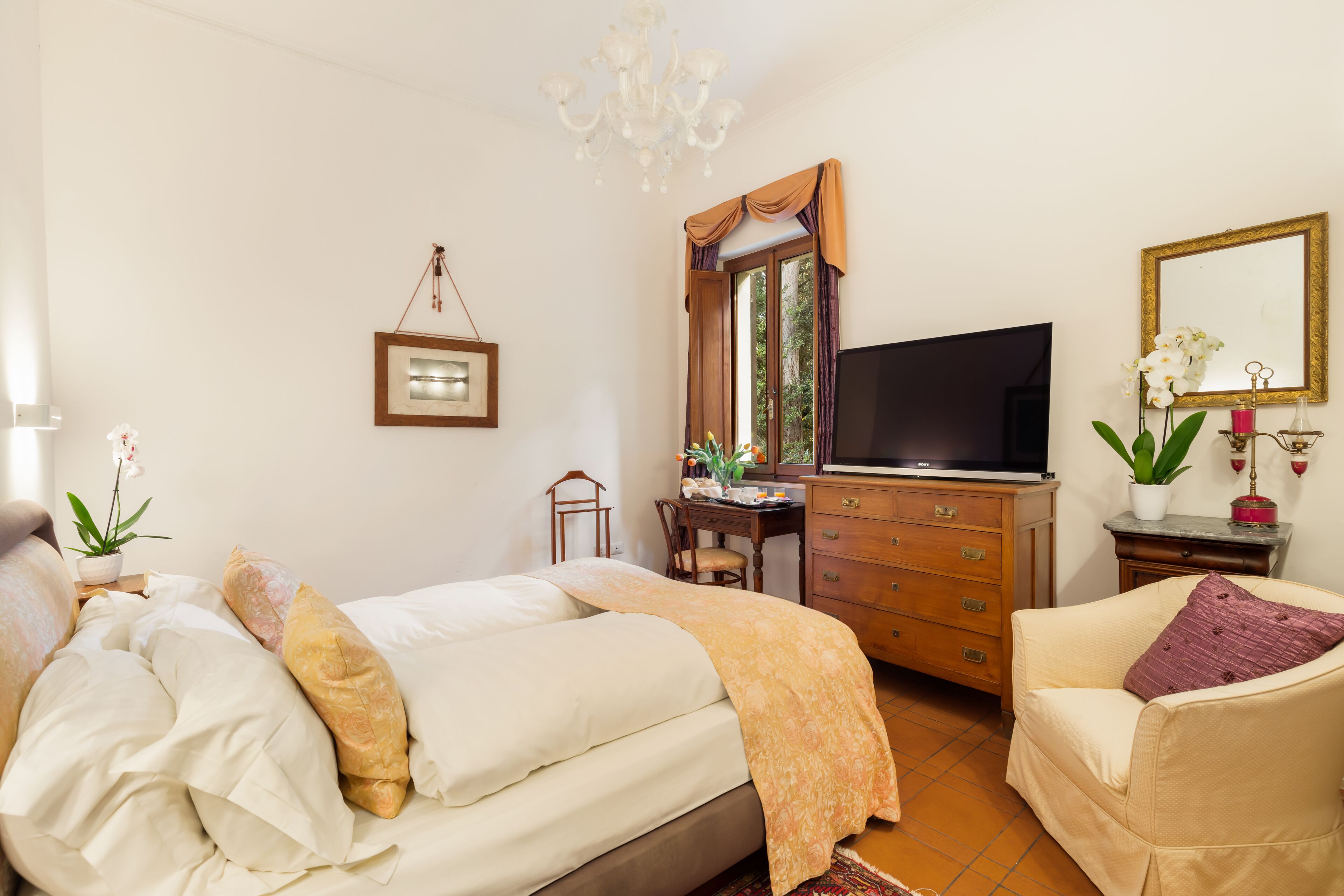 A bedroom with a bed, a desk, a television, a chair, and a dresser.