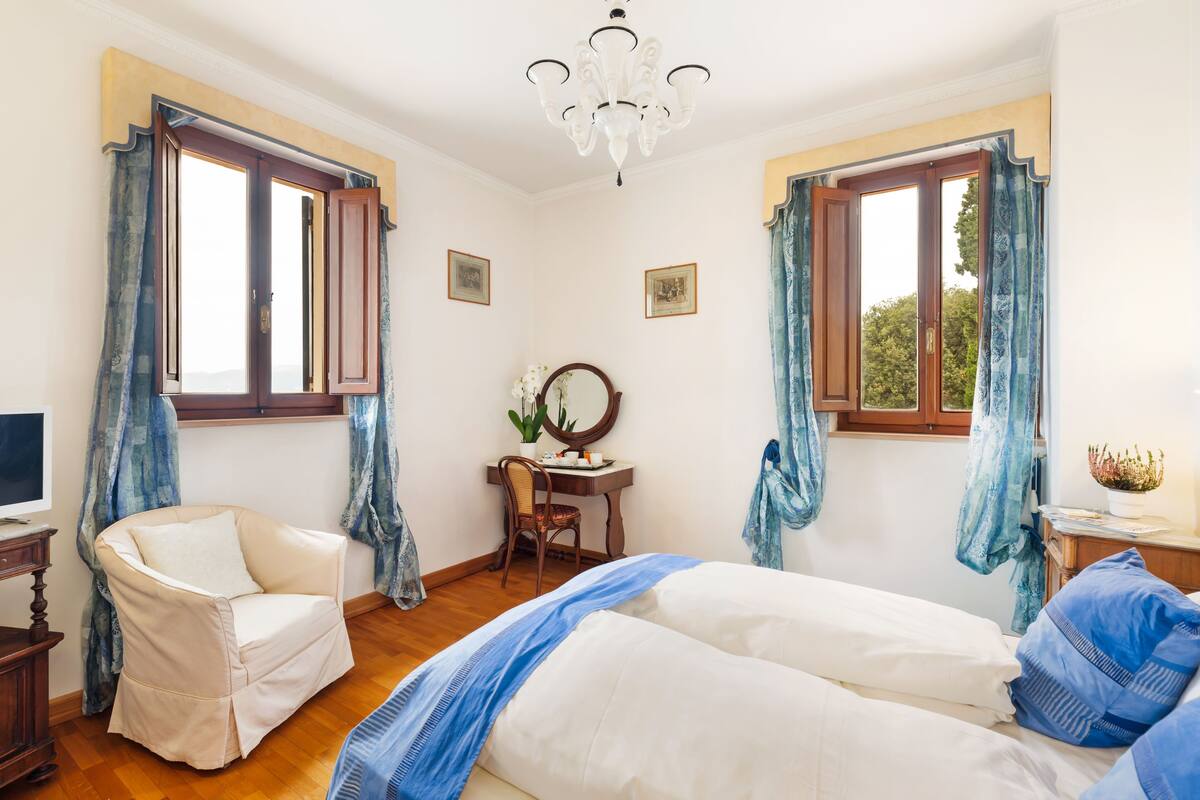 A bedroom with a bed, a chair, a desk, and a chandelier.