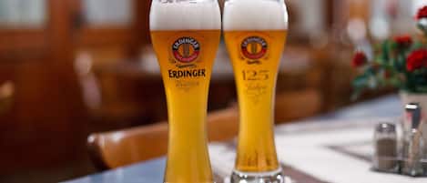 Two tall glasses of beer with the Erdinger Weihen logo on a table in a restaurant.