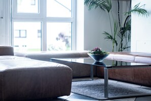 A modern living room with a sofa, a glass coffee table, and a potted plant. - Andante Hotel Erding (Erding)