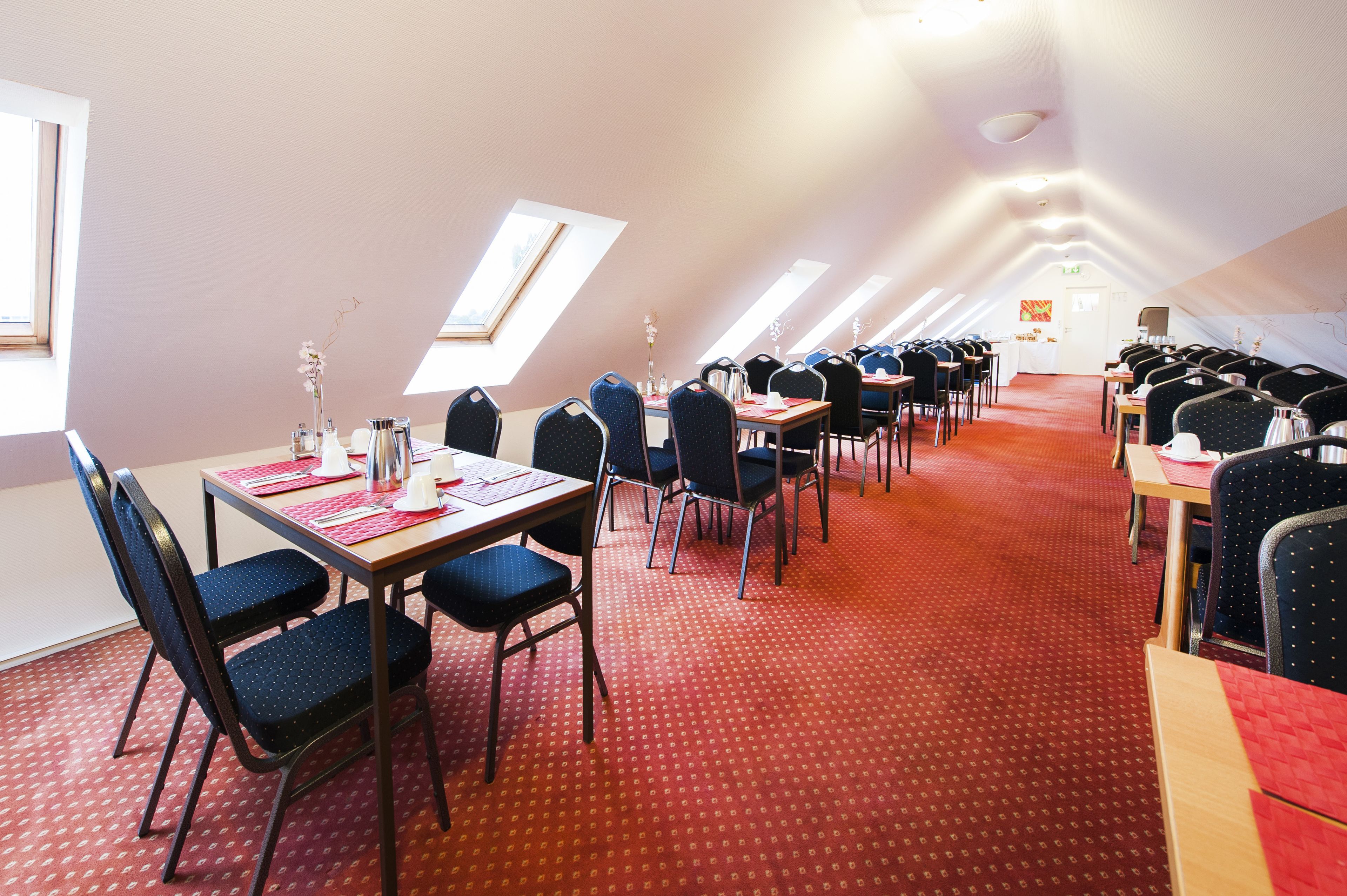 Ein Konferenzraum mit Tischen, Stühlen, hohen Decken und Dachfenstern.
