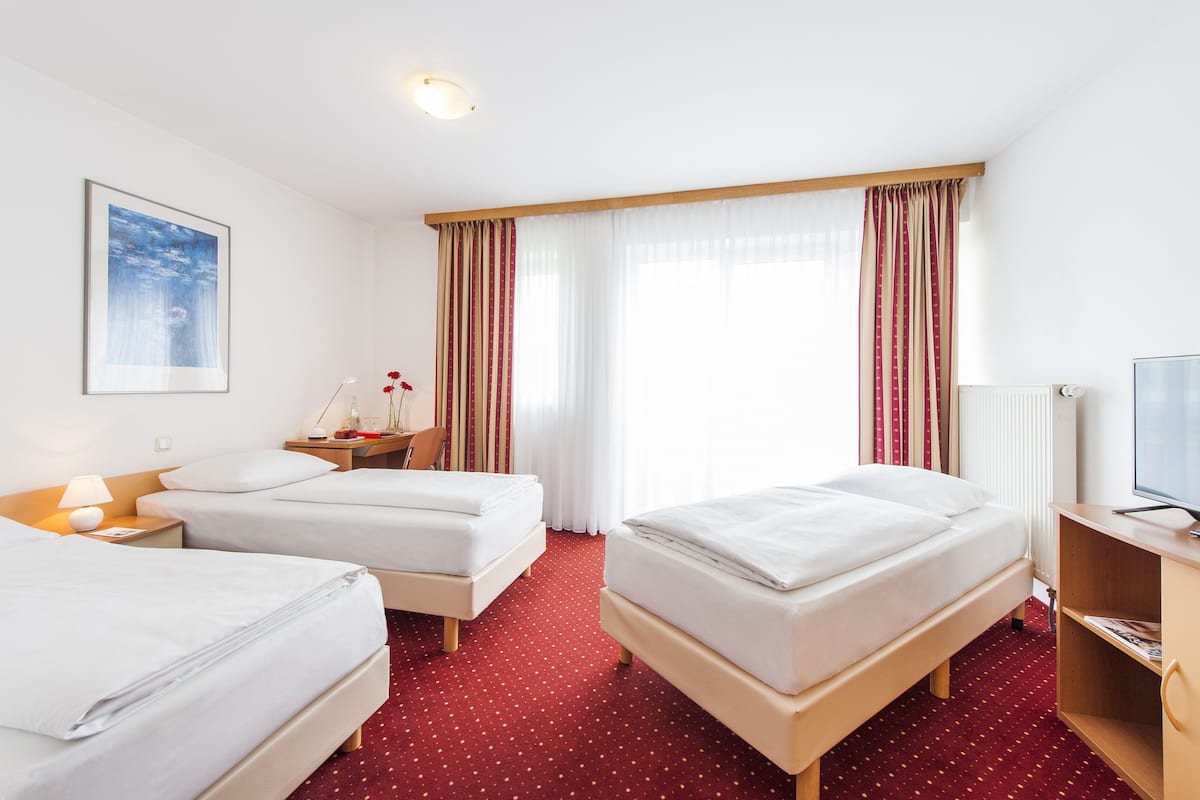 A hotel room with two beds, a TV, a lamp, a framed picture, and a window with curtains.
