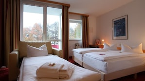 A hotel room with two beds, a sofa, and a large window with curtains.