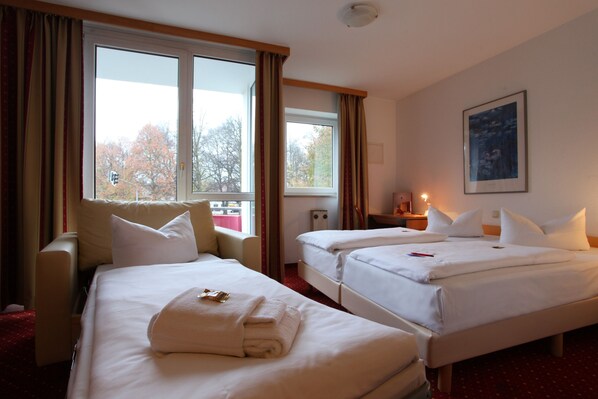 A hotel room with two beds, a sofa, and a large window with curtains. - Andante Hotel Erding (Erding)