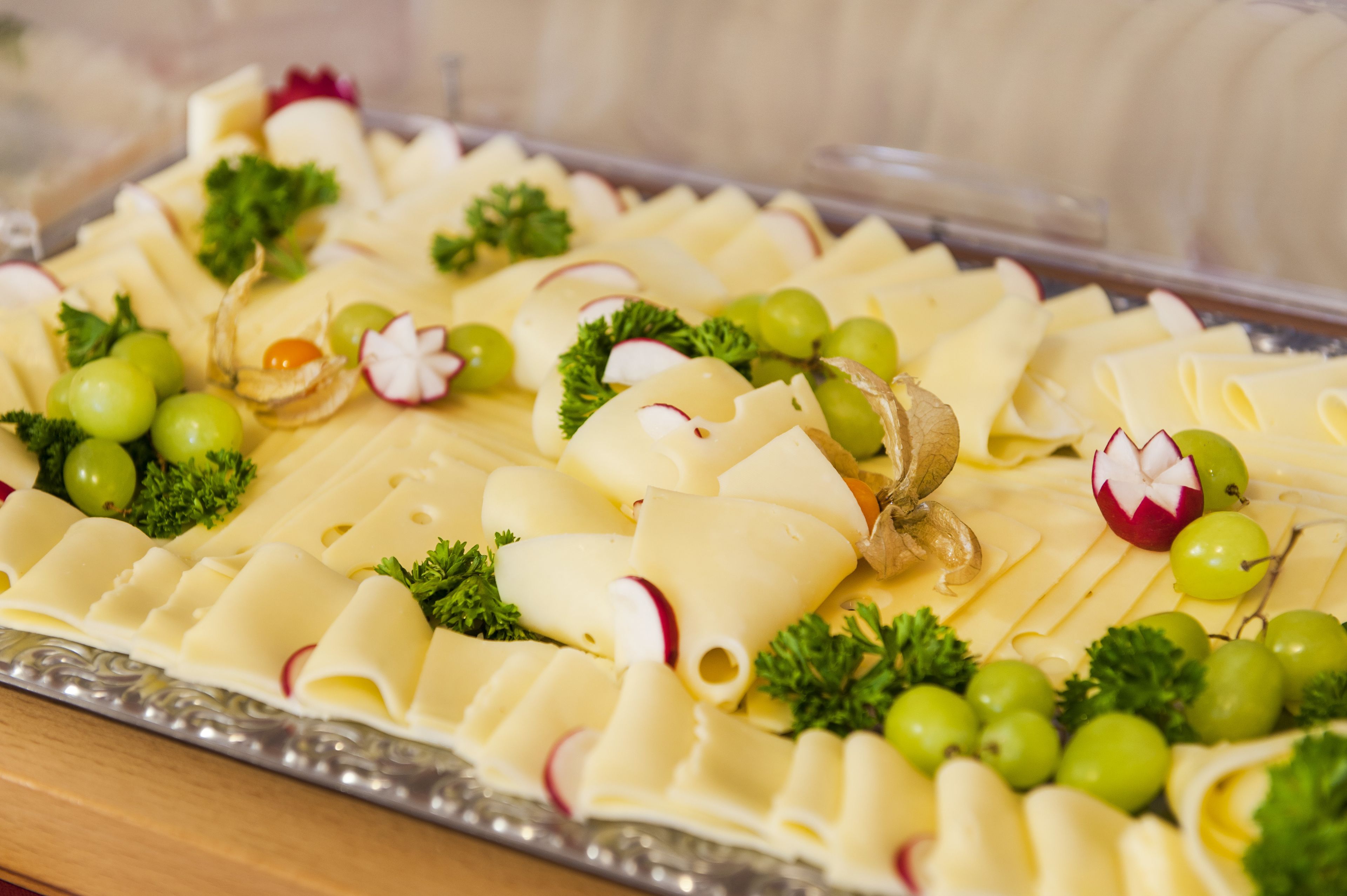 A platter of sliced cheese with grapes and radishes.