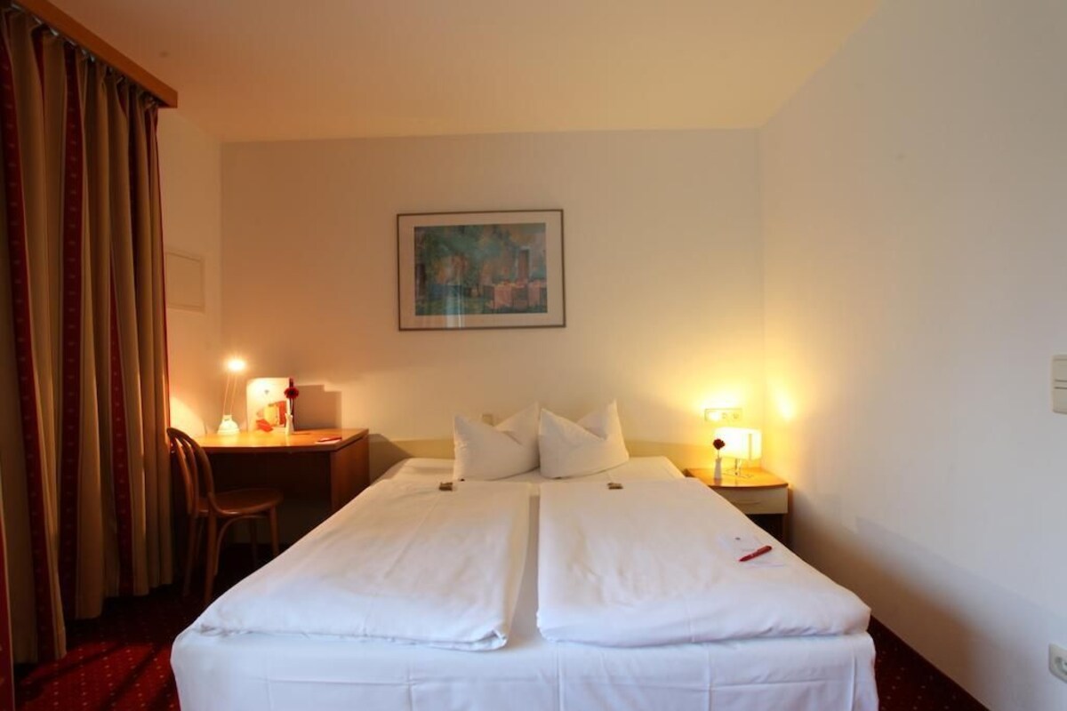 A hotel room with a bed, desk, chair, and two bedside lamps.