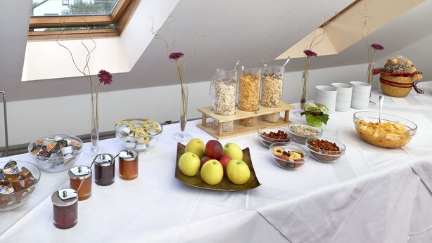 A buffet table with various food items and beverages, including fruits, nuts, and jars of preserves.