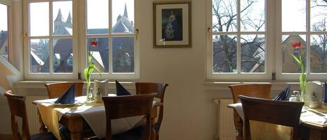 A dining room with a table set for four, large arched windows, and a framed painting on the wall.