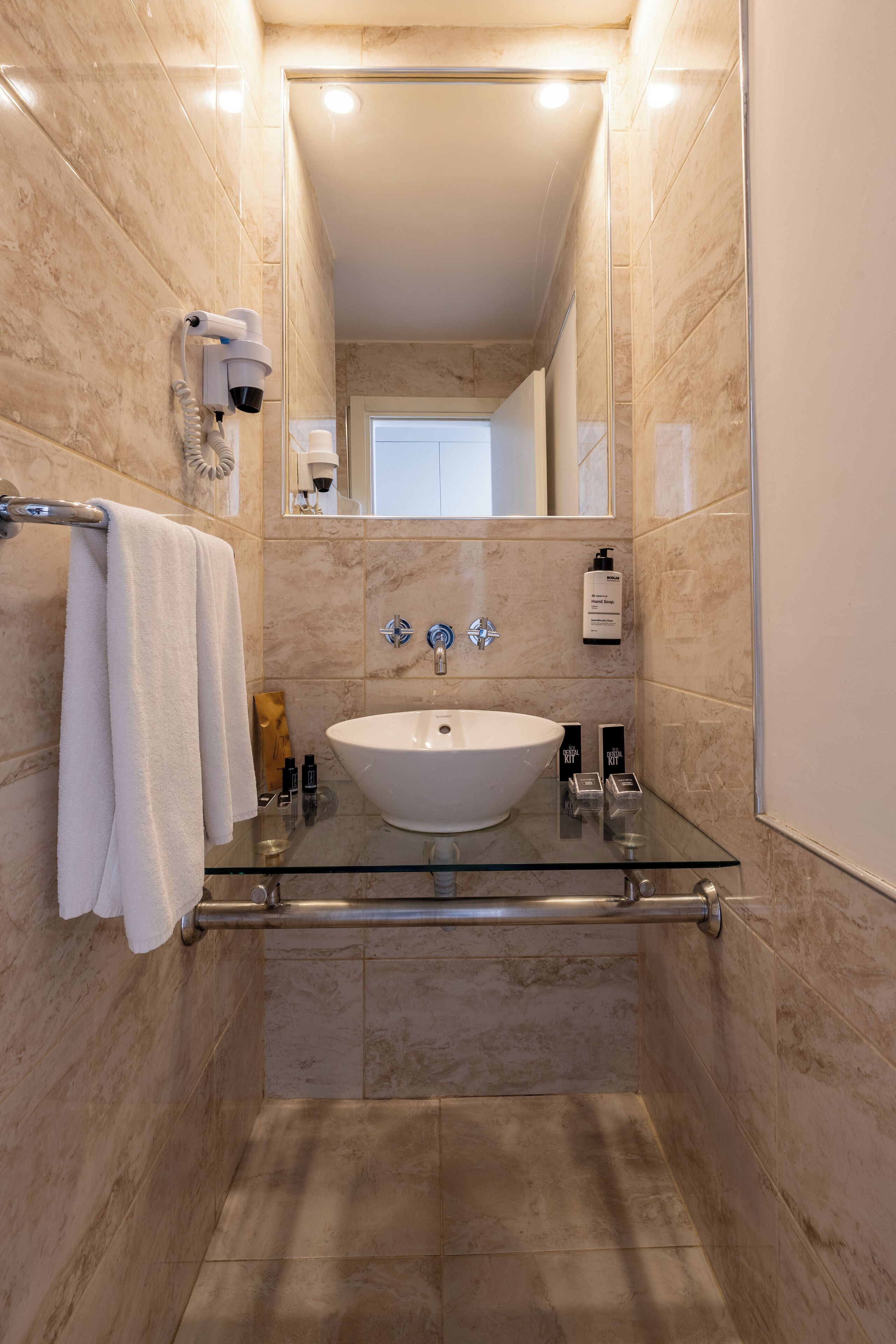 A modern bathroom with a glass-enclosed sink, a towel rack, a handheld showerhead, and a mirror.