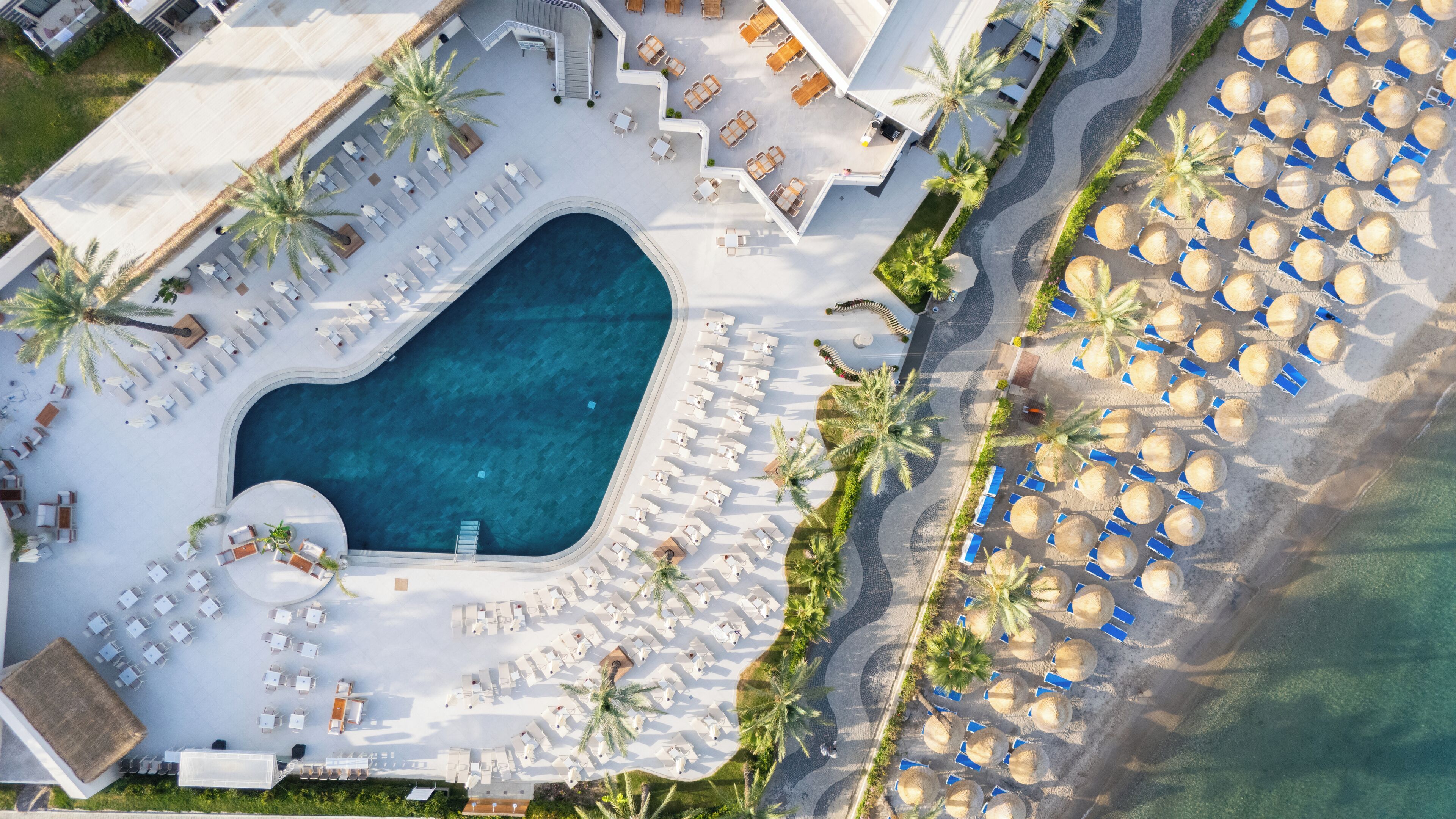 An aerial view of a resort with a swimming pool, sun loungers, and beach umbrellas.