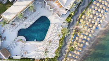 An aerial view of a resort with a swimming pool, sun loungers, and beach umbrellas.