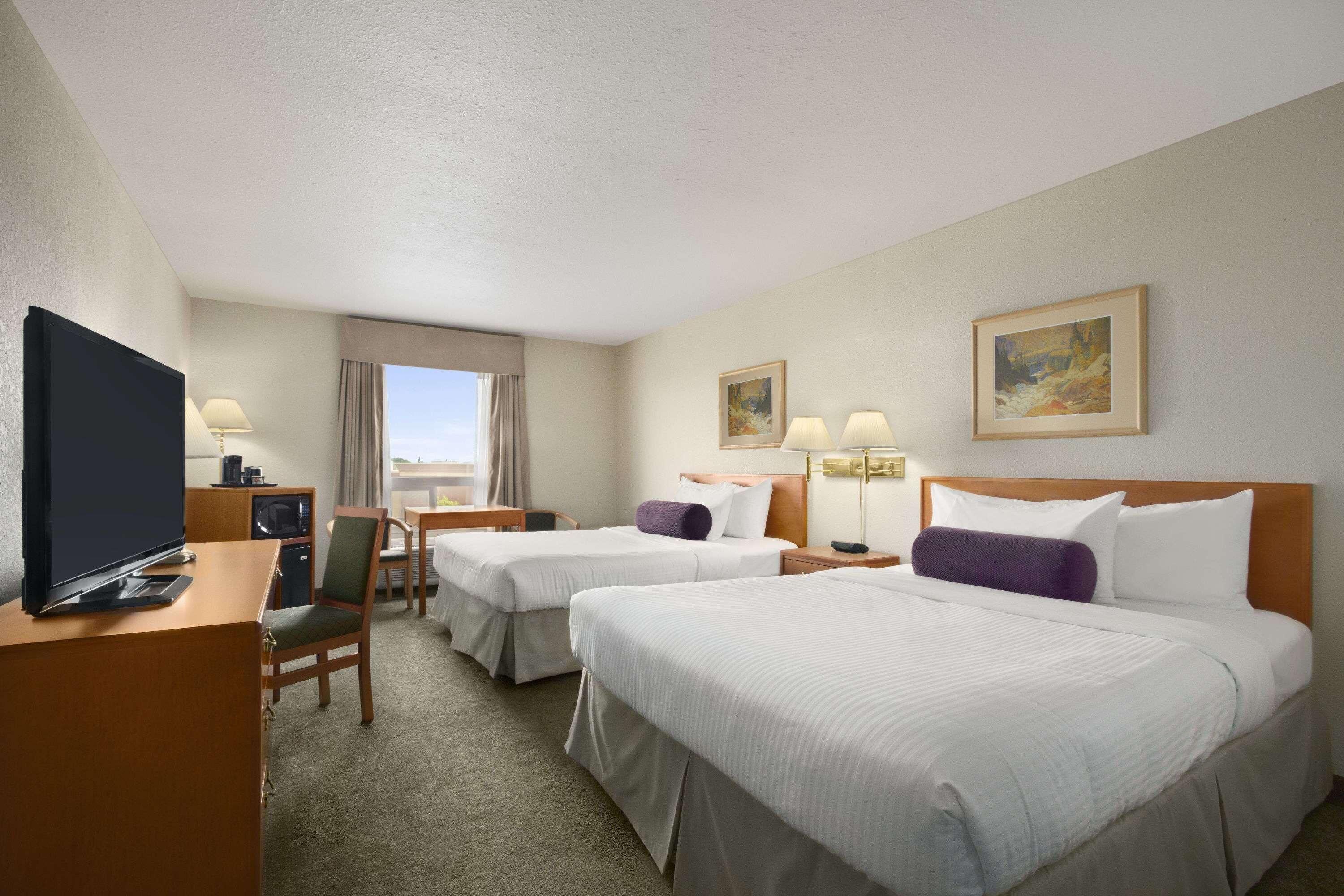 A hotel room with two beds, a desk with a TV, a chair, and a window with curtains.