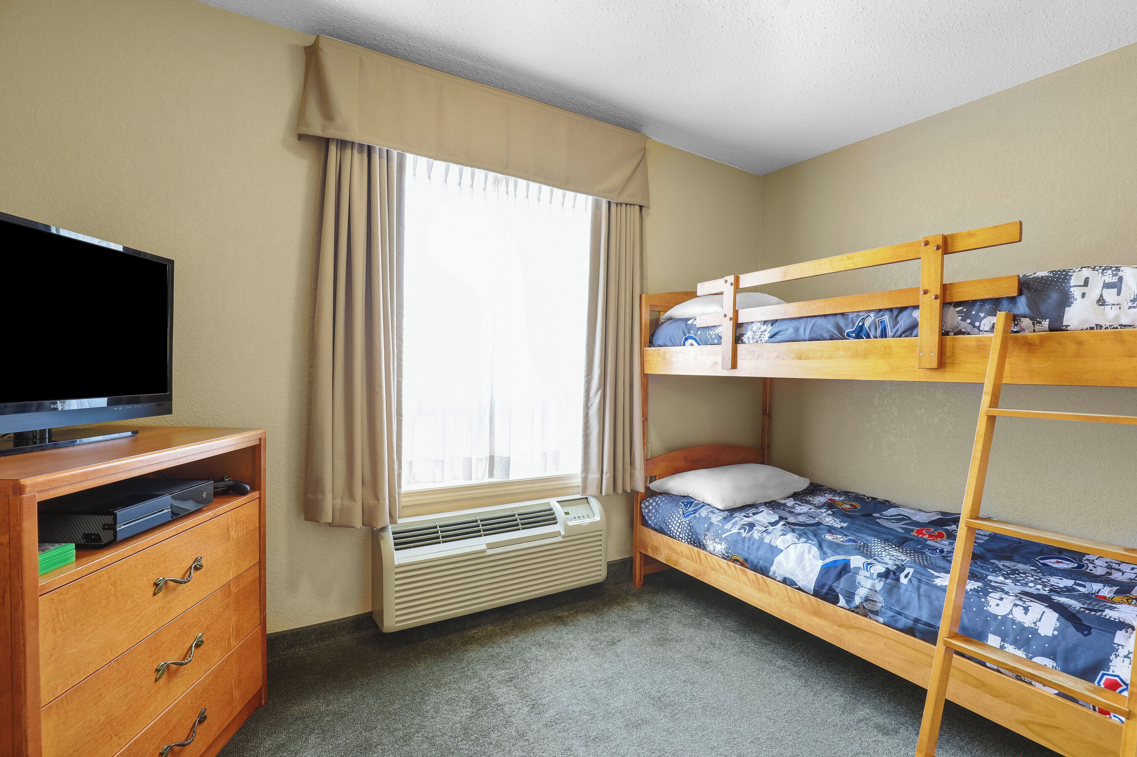 A room with a bunk bed, a television on a wooden cabinet, and a window with curtains.