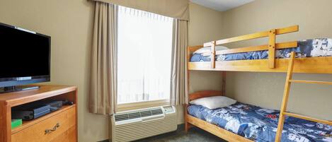 A room with a bunk bed, a television on a wooden cabinet, and a window with curtains.