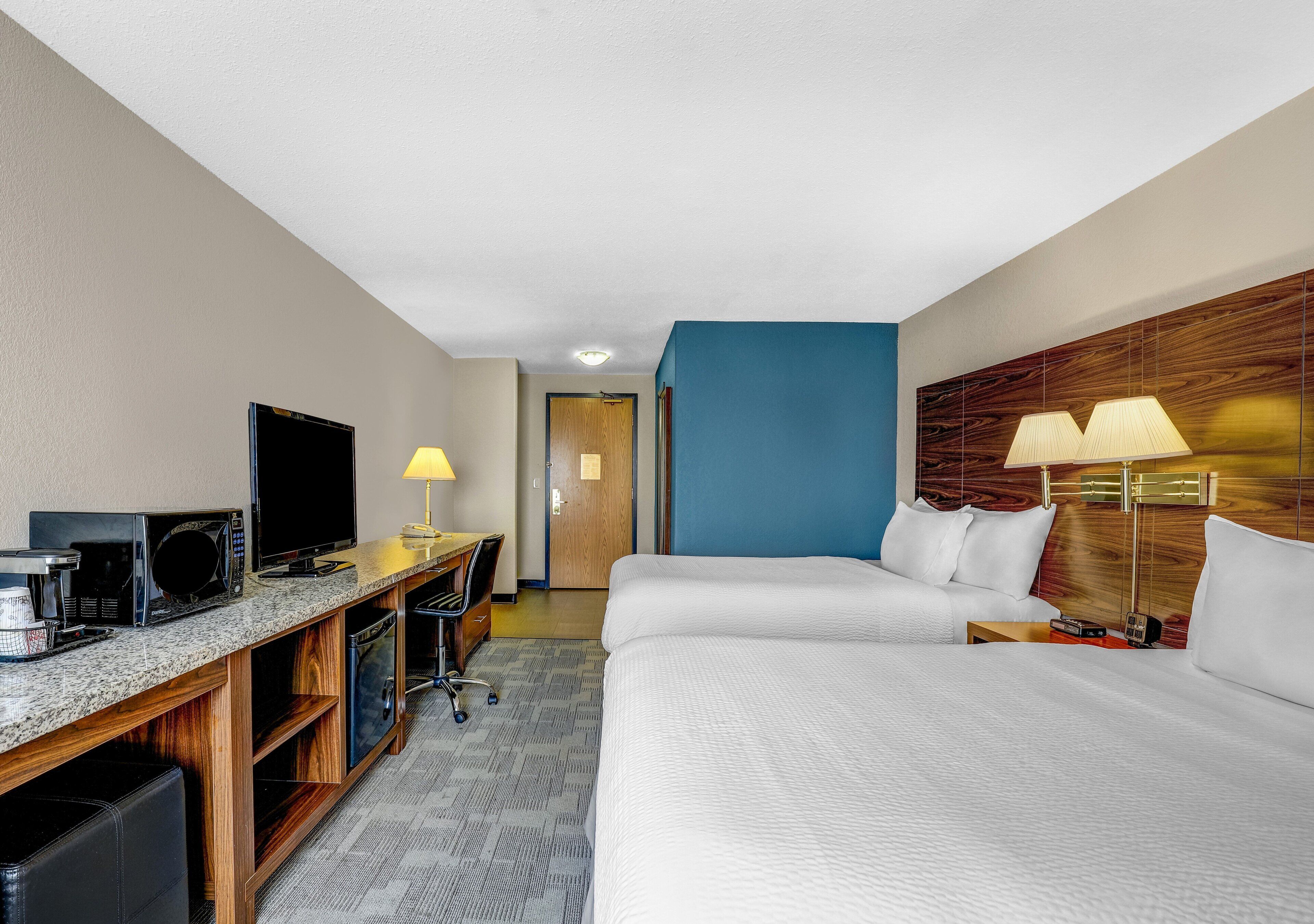 A hotel room with a bed, a desk with a TV, a lamp, and a microwave.