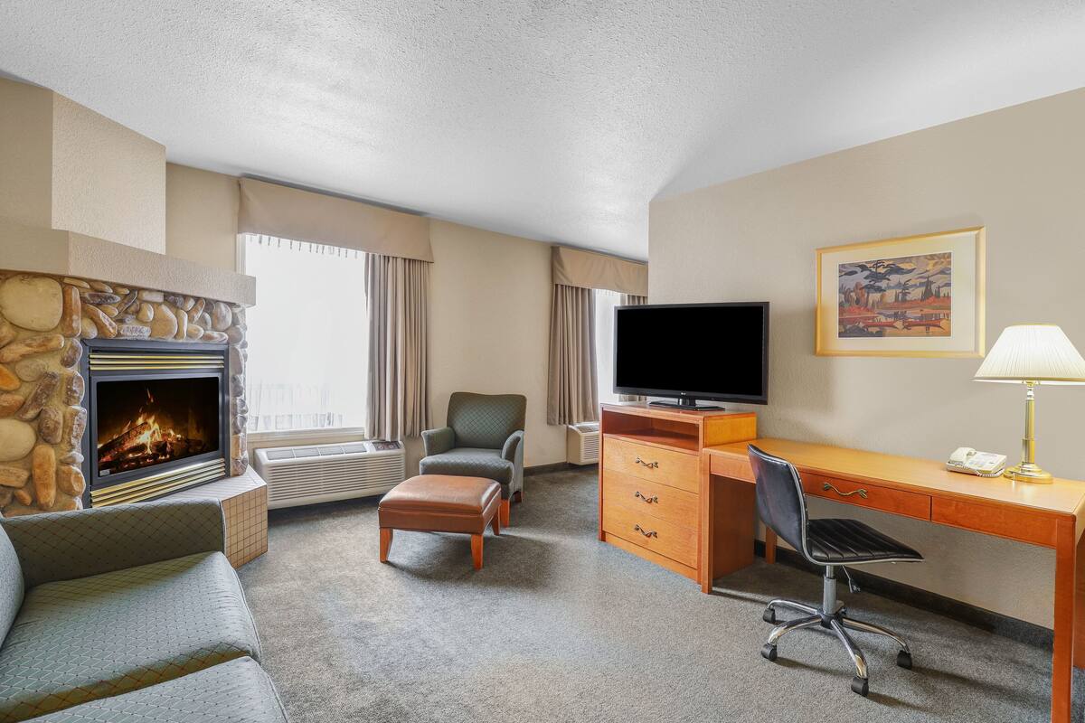 Ein Hotelzimmer mit Kamin, Fernseher, Schreibtisch mit Stuhl und einer Couch.