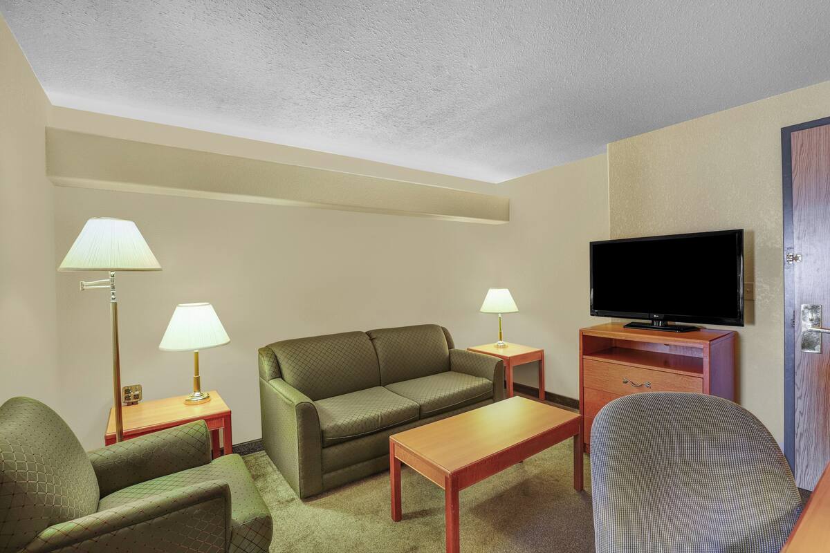 Ein Hotelzimmer mit einer Couch, zwei Lampen, einem Fernseher, einem Holztisch und einem Stuhl.
