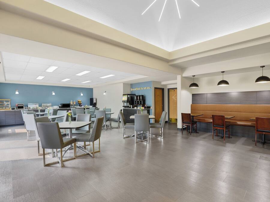 A modern dining area with tables and chairs, a counter with a coffee machine, and a sign that reads 'breakfast is on us.'