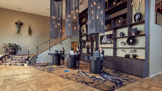 Un moderno vestíbulo de hotel con suelo de madera en espiga, una escalera y una recepción con personal.