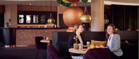 A modern dining area with a large copper vase centerpiece, dark wooden furniture, and pendant lighting.