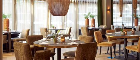 A dining area with round tables, cushioned chairs, and hanging woven light fixtures.