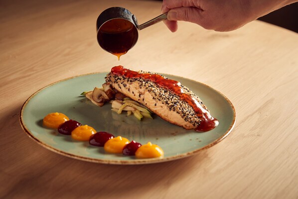 A plate with a piece of fish topped with sesame seeds and a sauce being poured over it. - Van der Valk Hotel Leusden - Amersfoort (Leusden-Centrum)