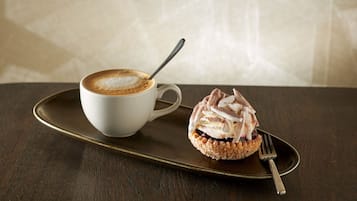 Una taza de café con una cuchara sobre una bandeja, acompañada de un pastel en un plato.
