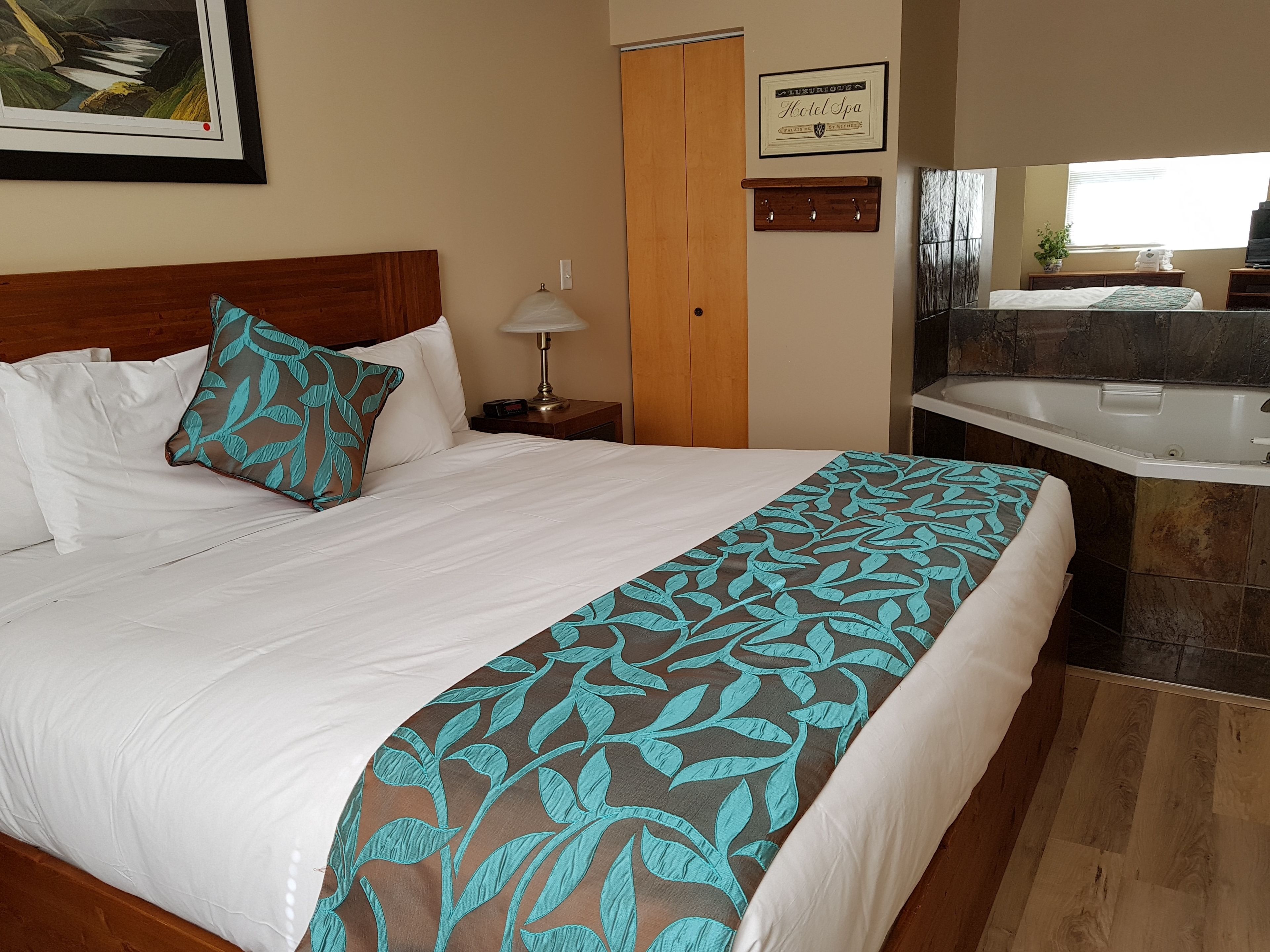 Habitación de hotel con una cama grande, cabecera de madera, mesita de noche con lámpara, baño con bañera y un cartel enmarcado en la pared.