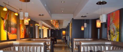 A modern restaurant interior with booth seating, pendant lighting, and colorful artwork on the walls.