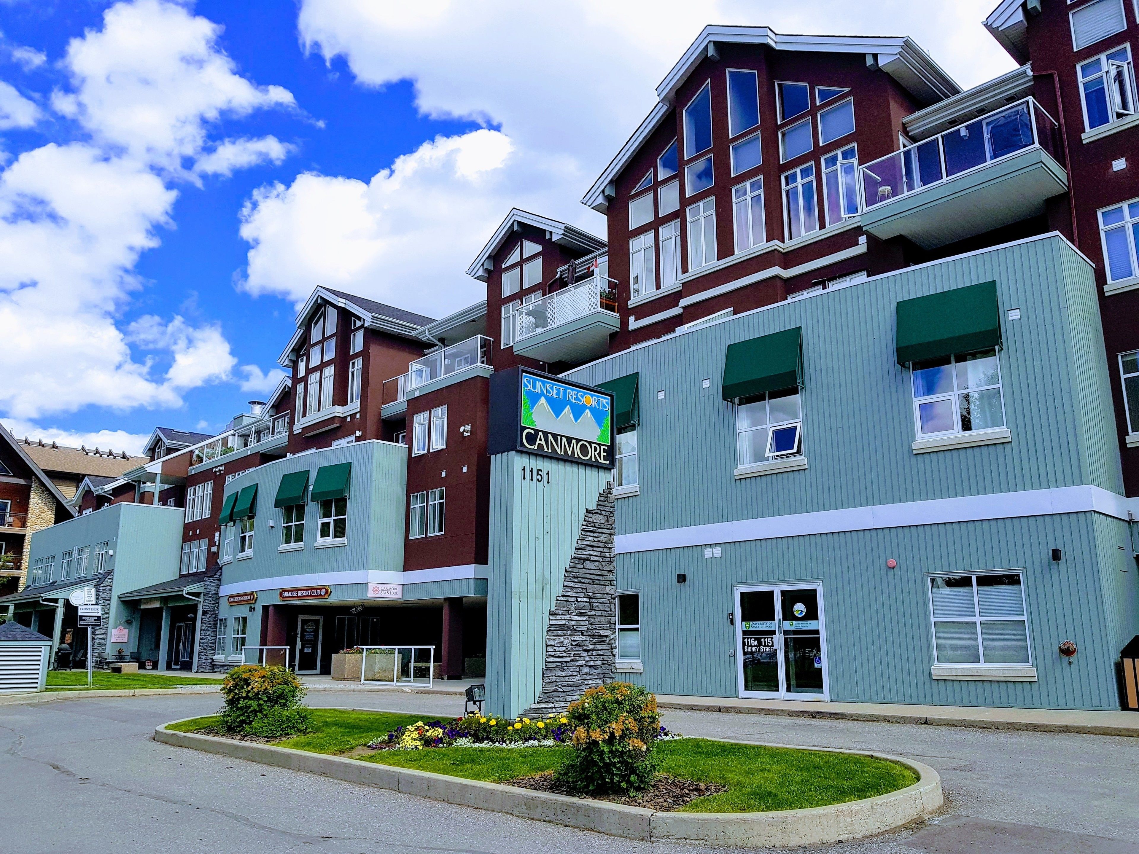 A multi-story building with a prominent 'Sunset Resorts' sign, a stone staircase, and a well-maintained lawn area.
