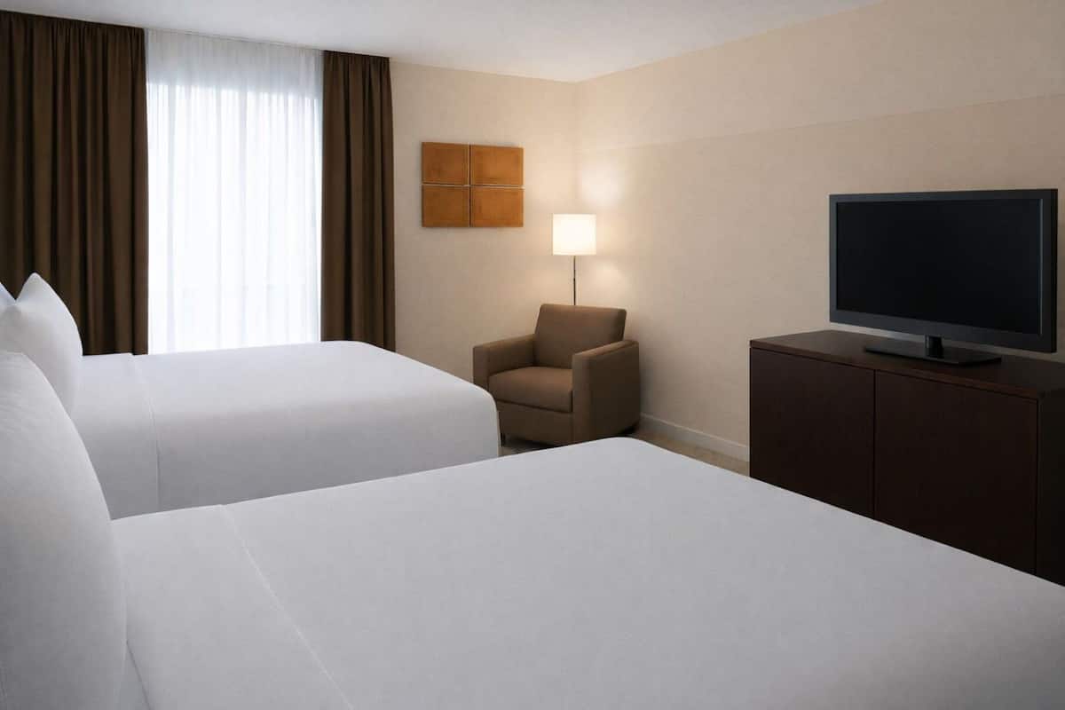 A hotel room with two beds, a TV on a cabinet, a lamp, and a wall-mounted artwork.