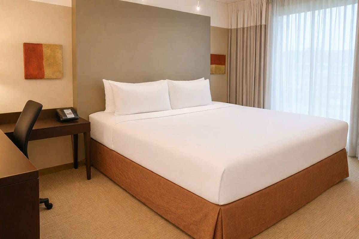 A hotel room with a large bed, a desk with a chair, and a telephone.