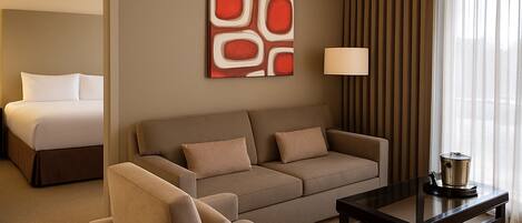 A hotel room with a bed, a sofa, a coffee table, and a lamp.
