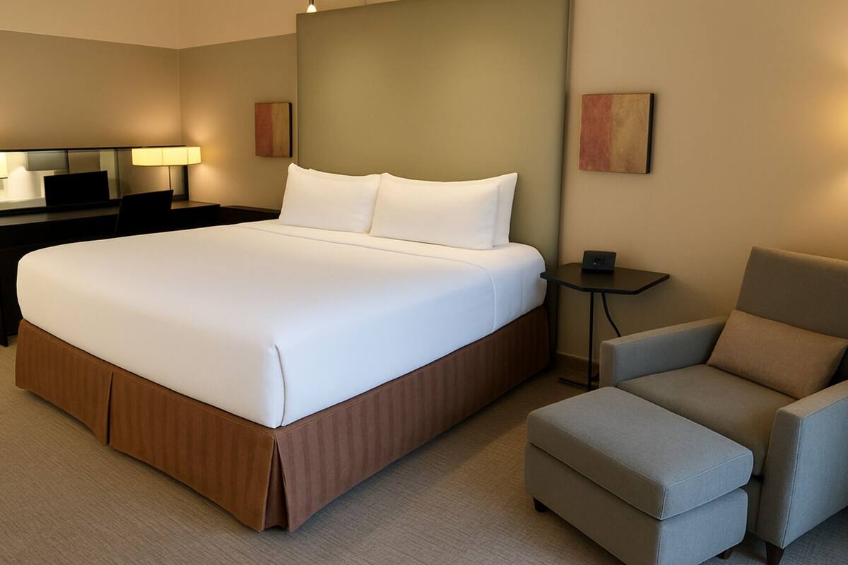 A hotel room with a large bed, a desk, a chair, and a small table.