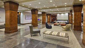 Un hall d’entrée spacieux agrémenté de hauts piliers en bois, d’un espace détente avec des canapés et un banc, d’un foyer et d’un design moderne.