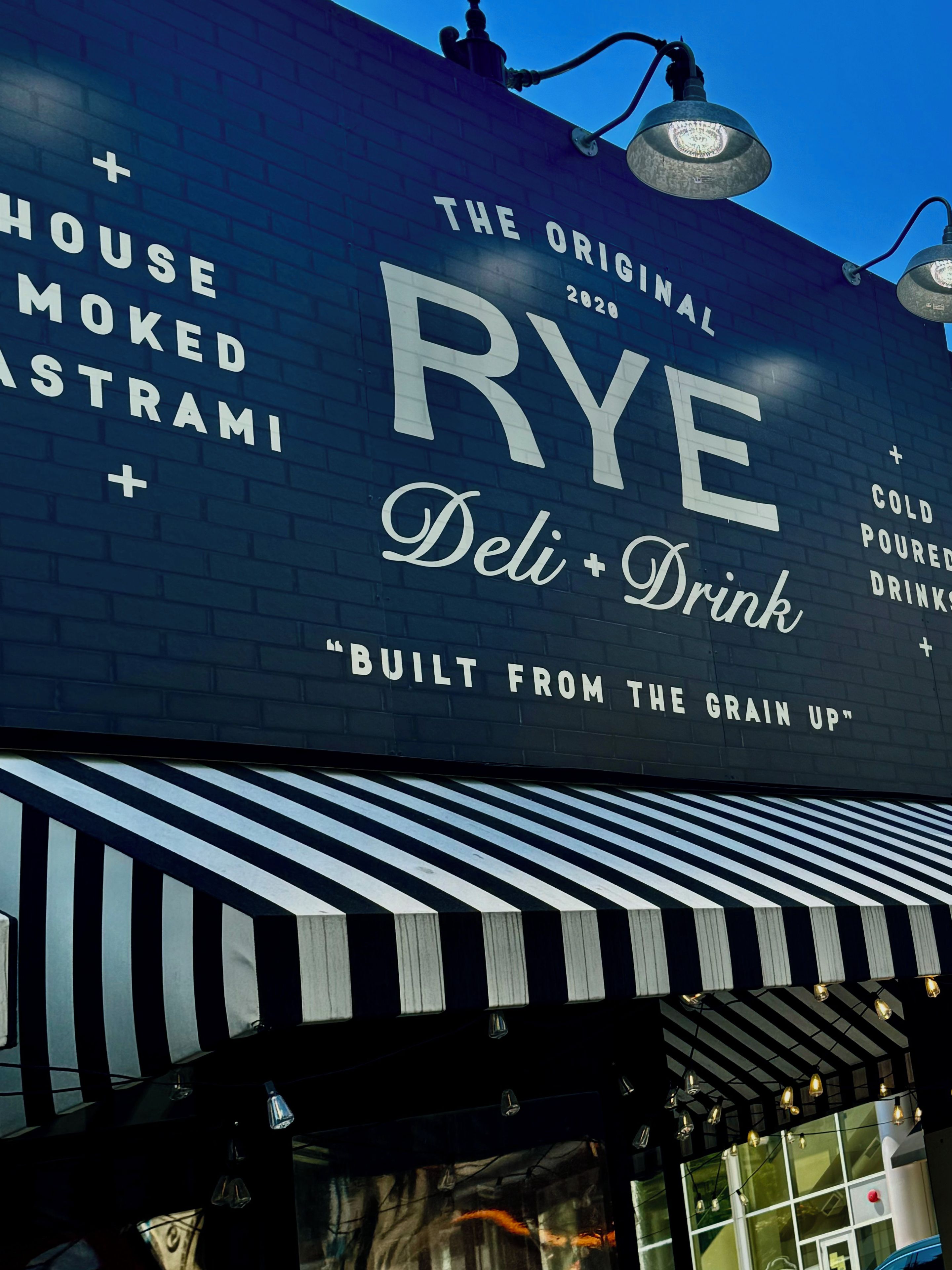 Um edifício com uma placa que diz 'RYE Deli + Drink' e 'Construído a partir do Grão'.