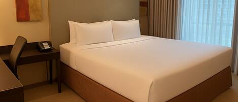 A hotel room with a large bed, a desk with a telephone, and a window with curtains.