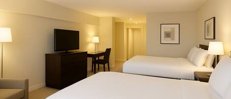 A hotel room with two beds, a desk, a TV, and a chair.