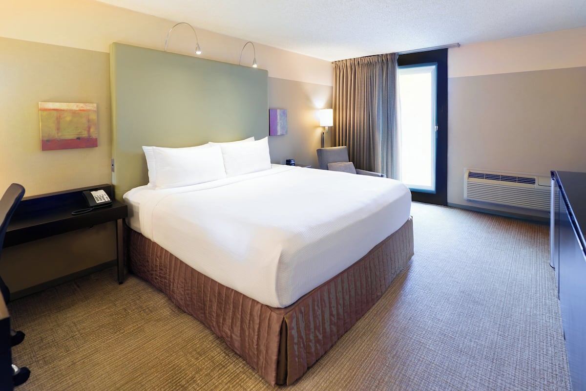 A hotel room with a large bed, a desk, a chair, a desk lamp, and a window with curtains.