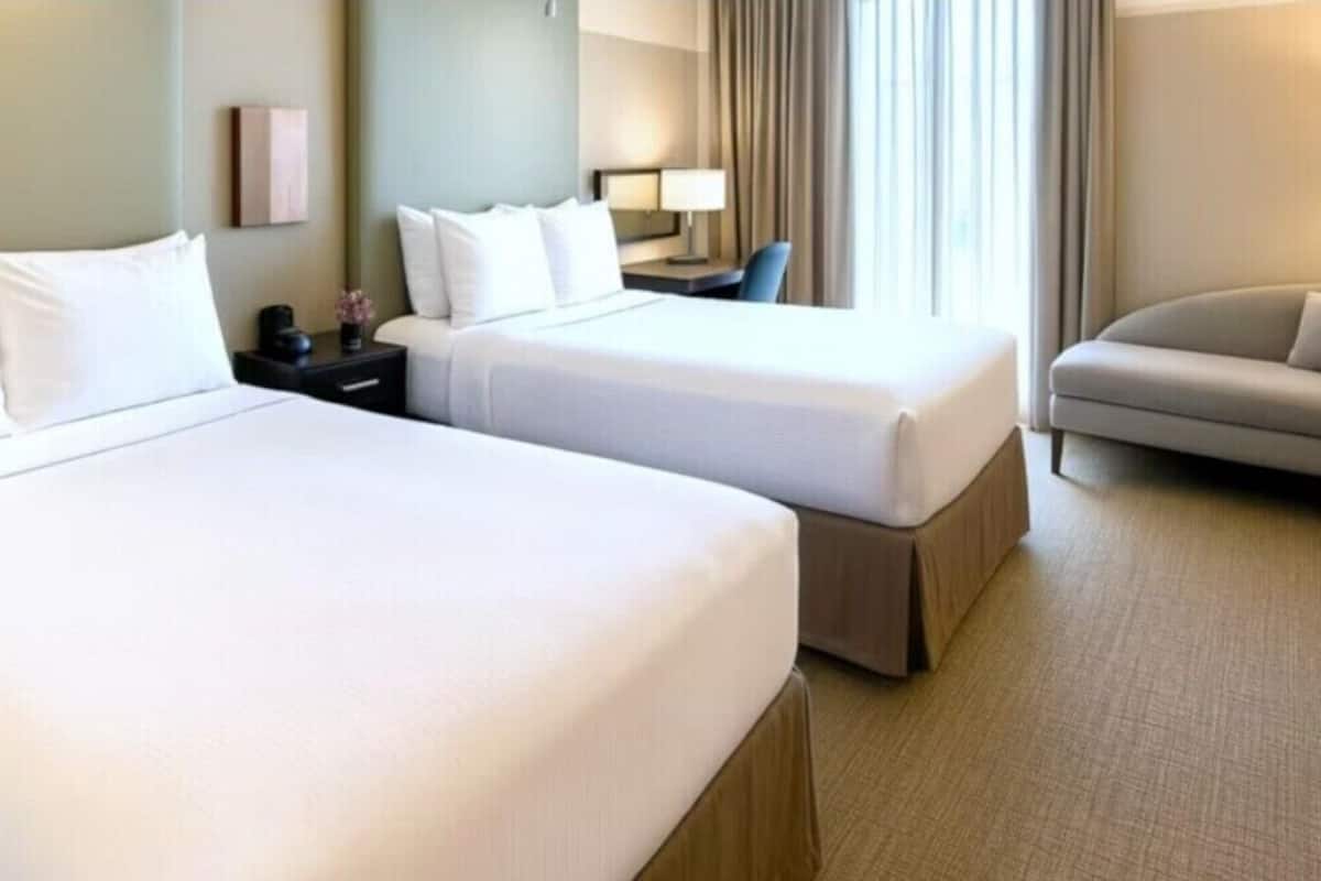 A hotel room with two beds, a sofa, a nightstand, a lamp, and a window with curtains.