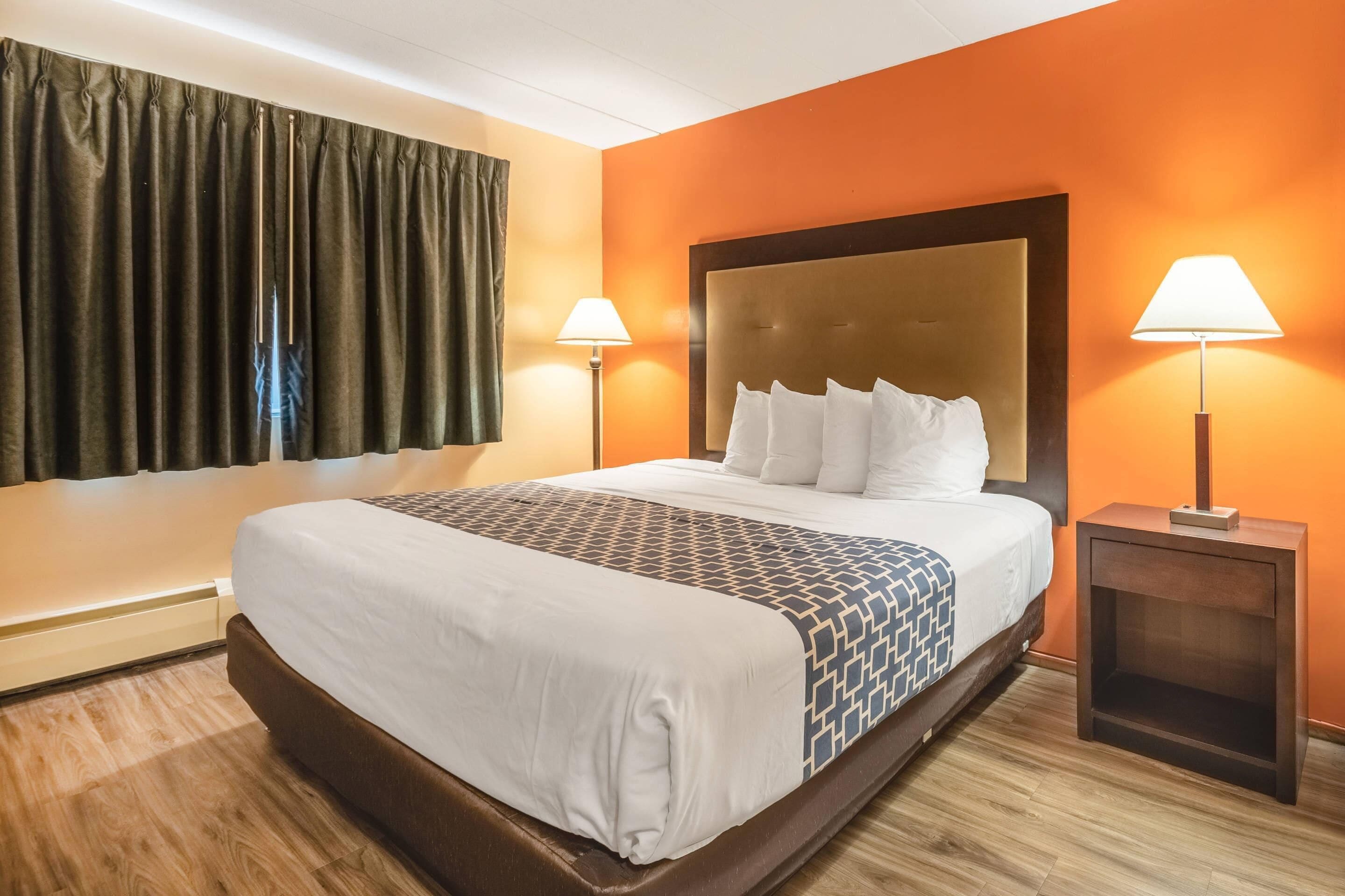 A hotel room with a large bed, two bedside lamps, a headboard, and a window with curtains.
