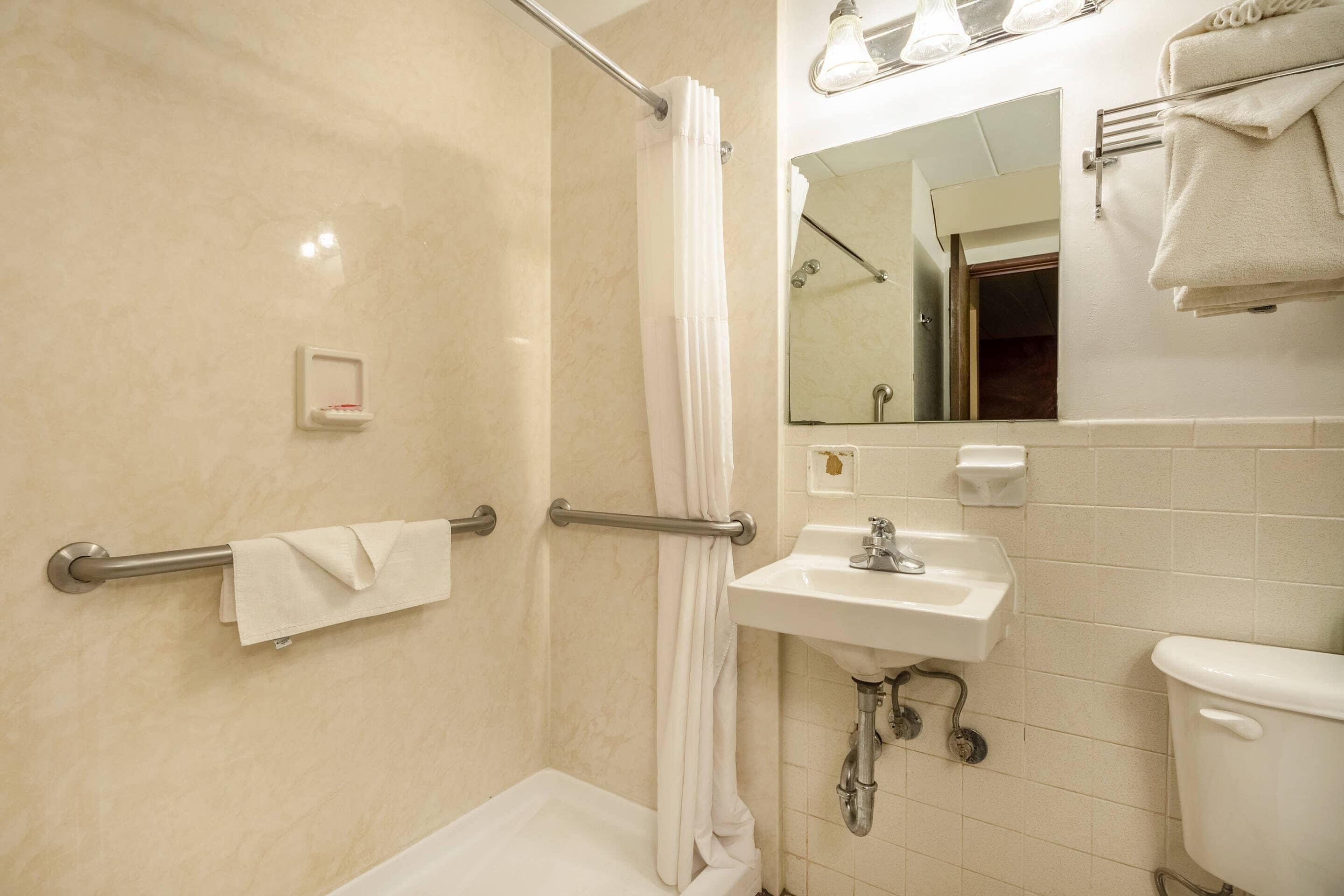 Un baño con ducha, lavamanos, inodoro, toallero y espejo.