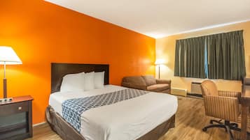 A hotel room with a large bed, a desk, a chair, and two lamps.