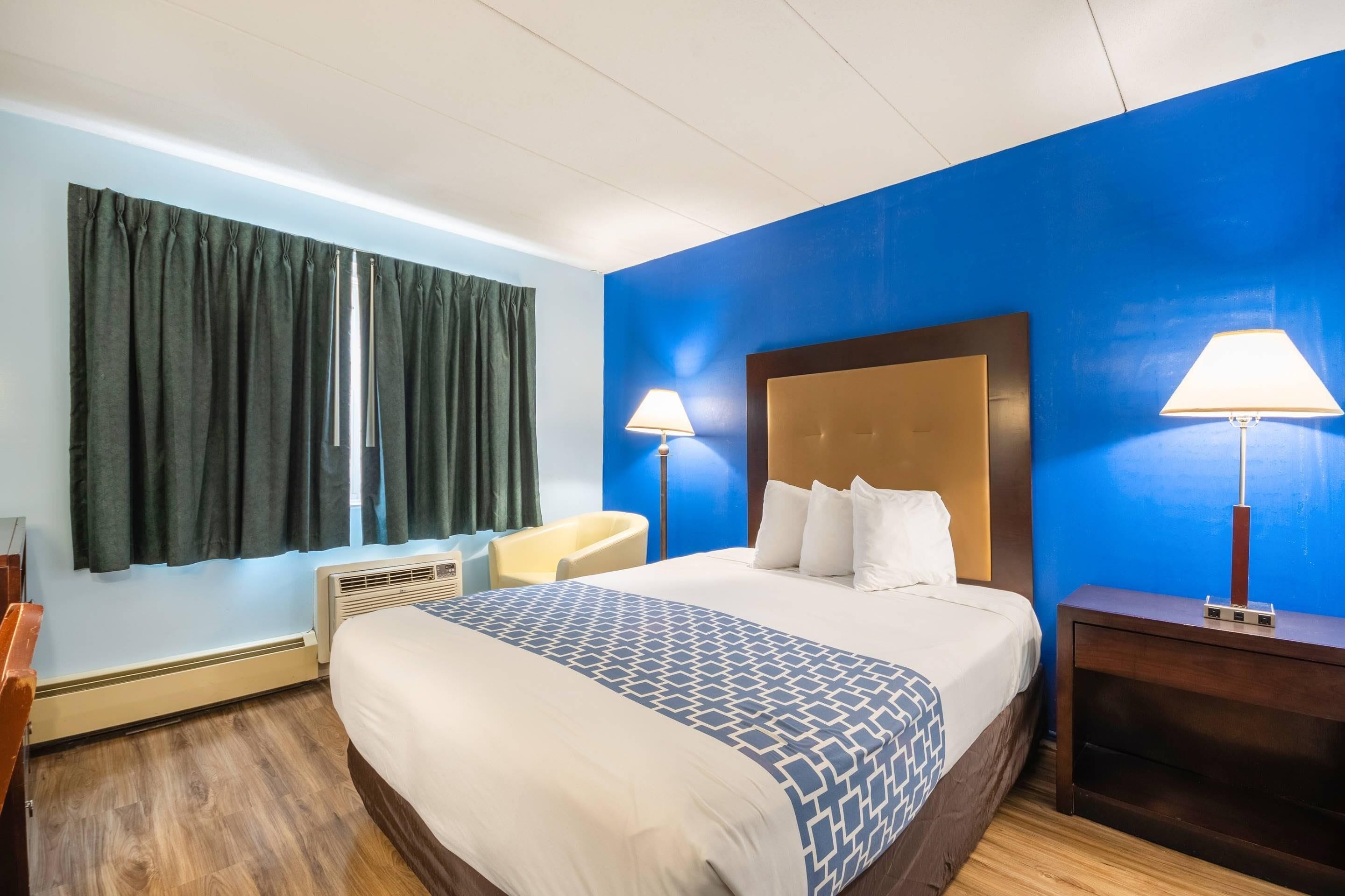 Une chambre d’hôtel avec un grand lit, deux lampes de chevet, une chaise, un bureau et une fenêtre avec des rideaux.
