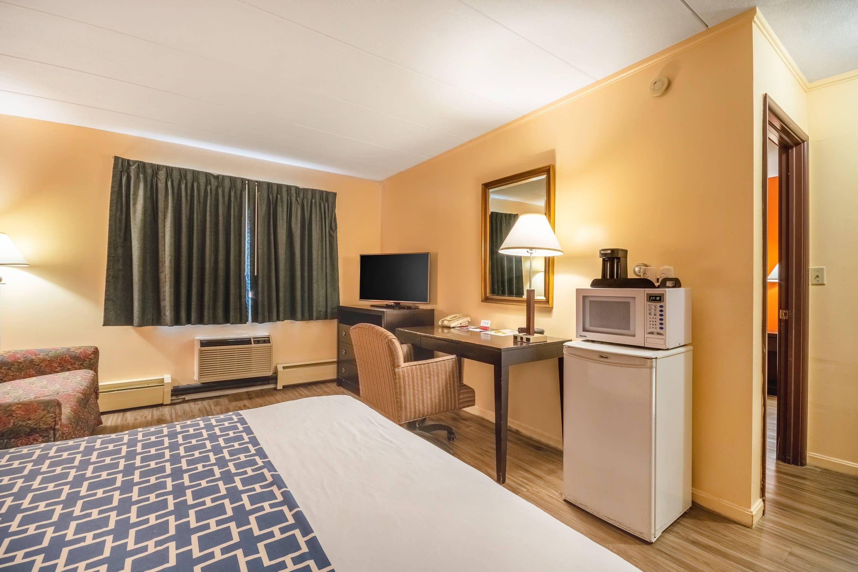 A hotel room with a bed, a desk with a computer, a television, a microwave, and a chair.