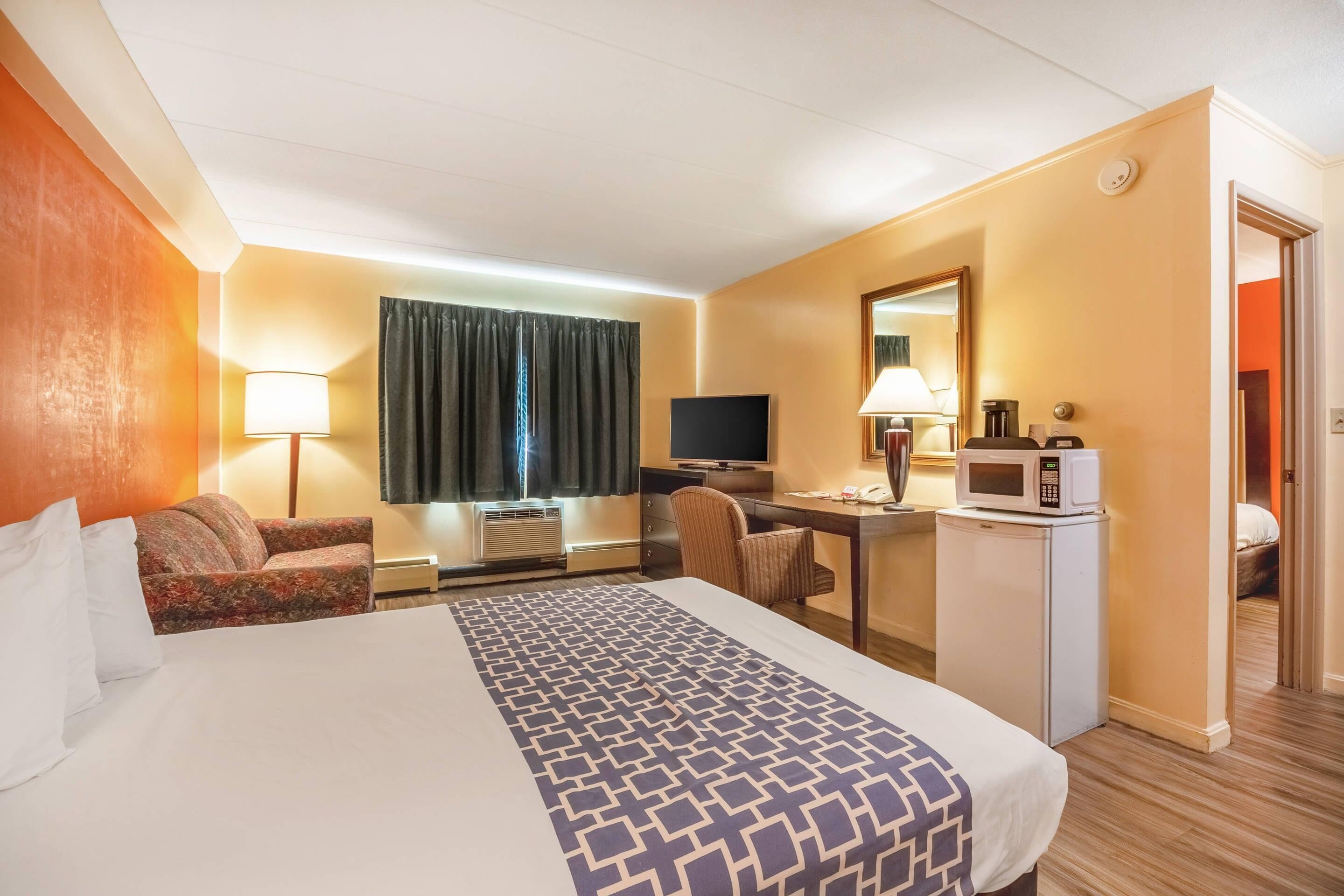 Habitación de hotel con una cama grande, un escritorio con computadora, televisión, microondas y refrigerador pequeño.